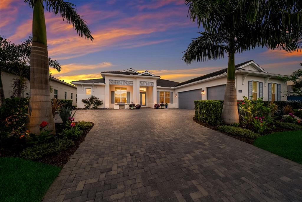 A single-story house with a paved driveway and palm trees under a sunset sky — 8448 CANE BAY COURT, LAKEWOOD RANCH, FL