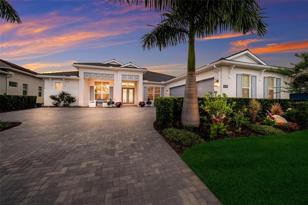 A single-story house with a paved driveway, palm tree, and landscaped garden at sunset — 8448 CANE BAY COURT, LAKEWOOD RANCH, FL