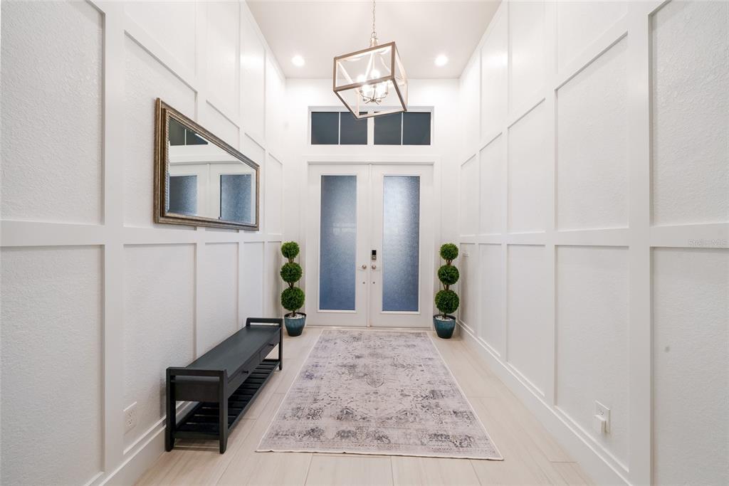 A bright entryway features white board and batten walls, a dark bench, and a chandelier — 8448 CANE BAY COURT, LAKEWOOD RANCH, FL