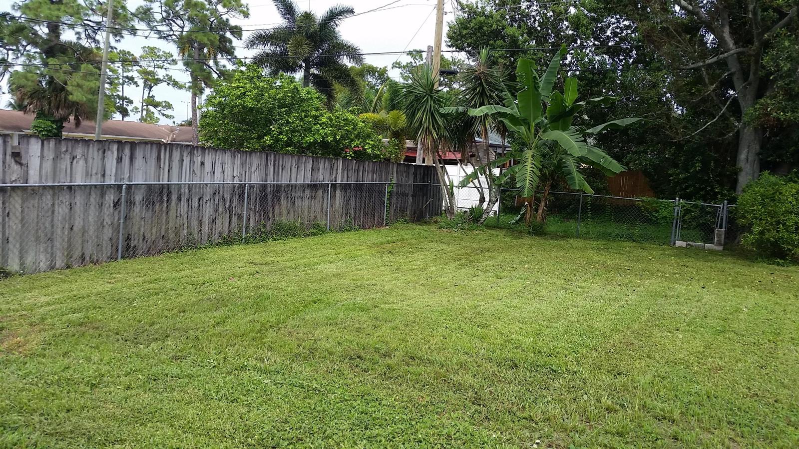 A grassy backyard features a wooden privacy fence, a chain-link fence, and various tropical plants — 460 Fleming Avenue, FL 33467, FL