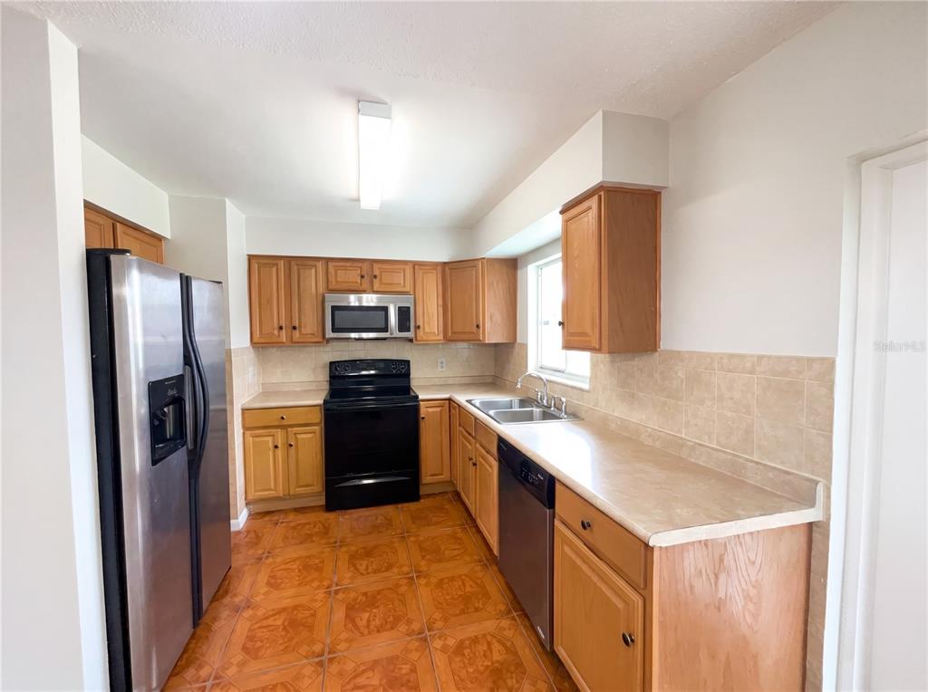 A kitchen with wood cabinets, stainless steel appliances, tile flooring, and a beige laminate countertop — 4805 BEACON STREET, ORLANDO, FL