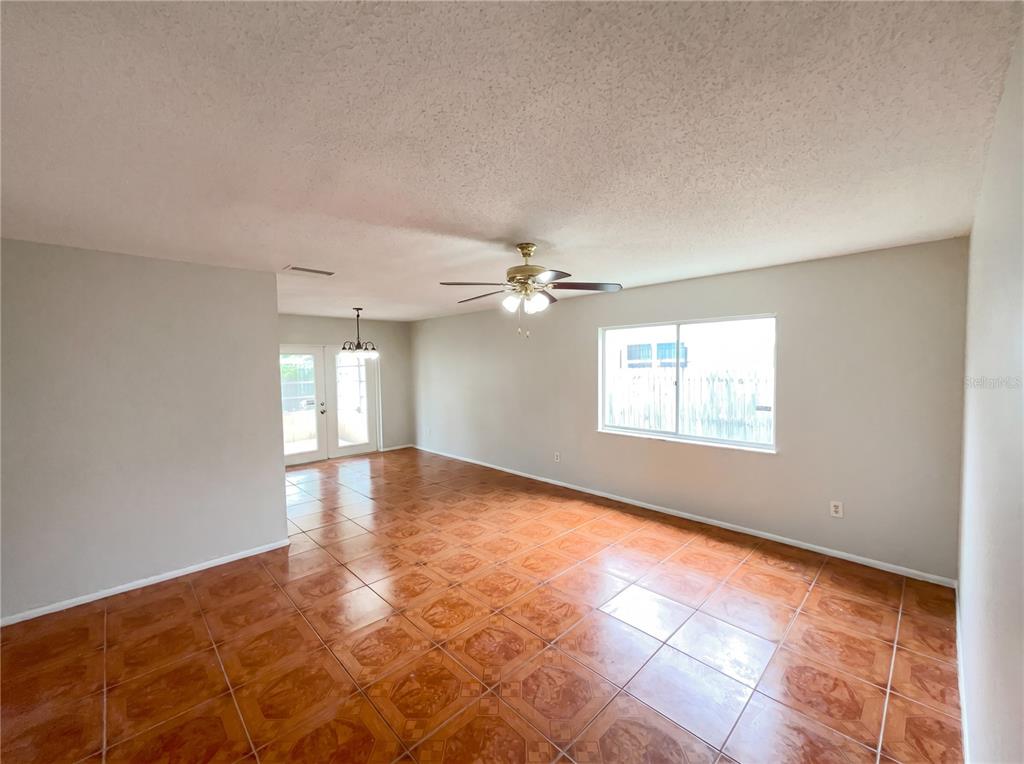An empty room features tan tile flooring, a ceiling fan, and a large window — 4805 BEACON STREET, ORLANDO, FL