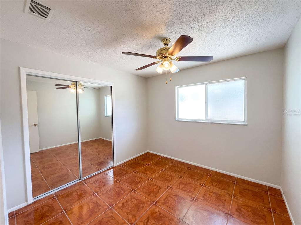 A bedroom features light-colored walls, a ceiling fan, a mirrored closet, and brown tile flooring — 4805 BEACON STREET, ORLANDO, FL