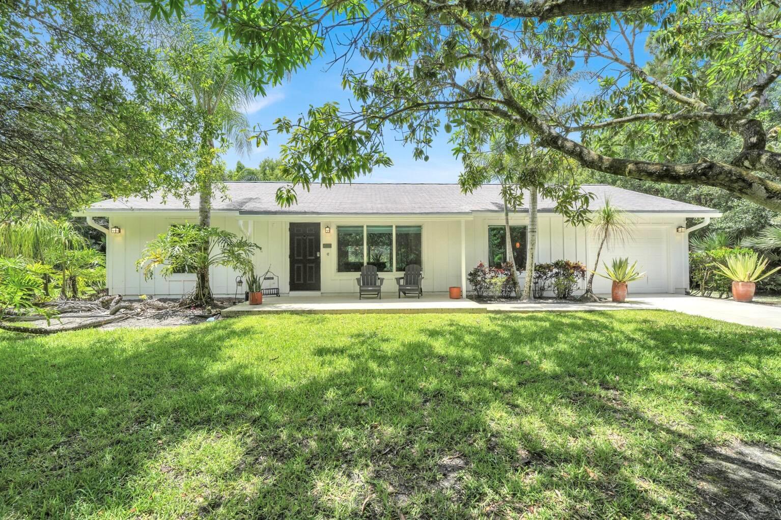 A white single-story house with a front porch, dark door, and large lawn under trees — 12216 184th Court N, Jupiter FL 33478, JUPITER, FL