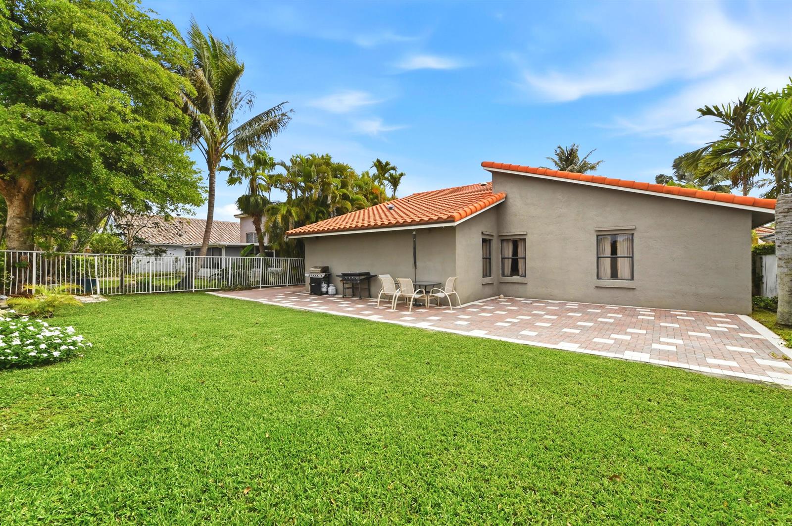 A backyard features a paved patio, a grassy lawn, and a house with a tiled roof — 263 NW 48th Avenue, Deerfield Beach FL 33442, DEERFIELD BEACH, FL