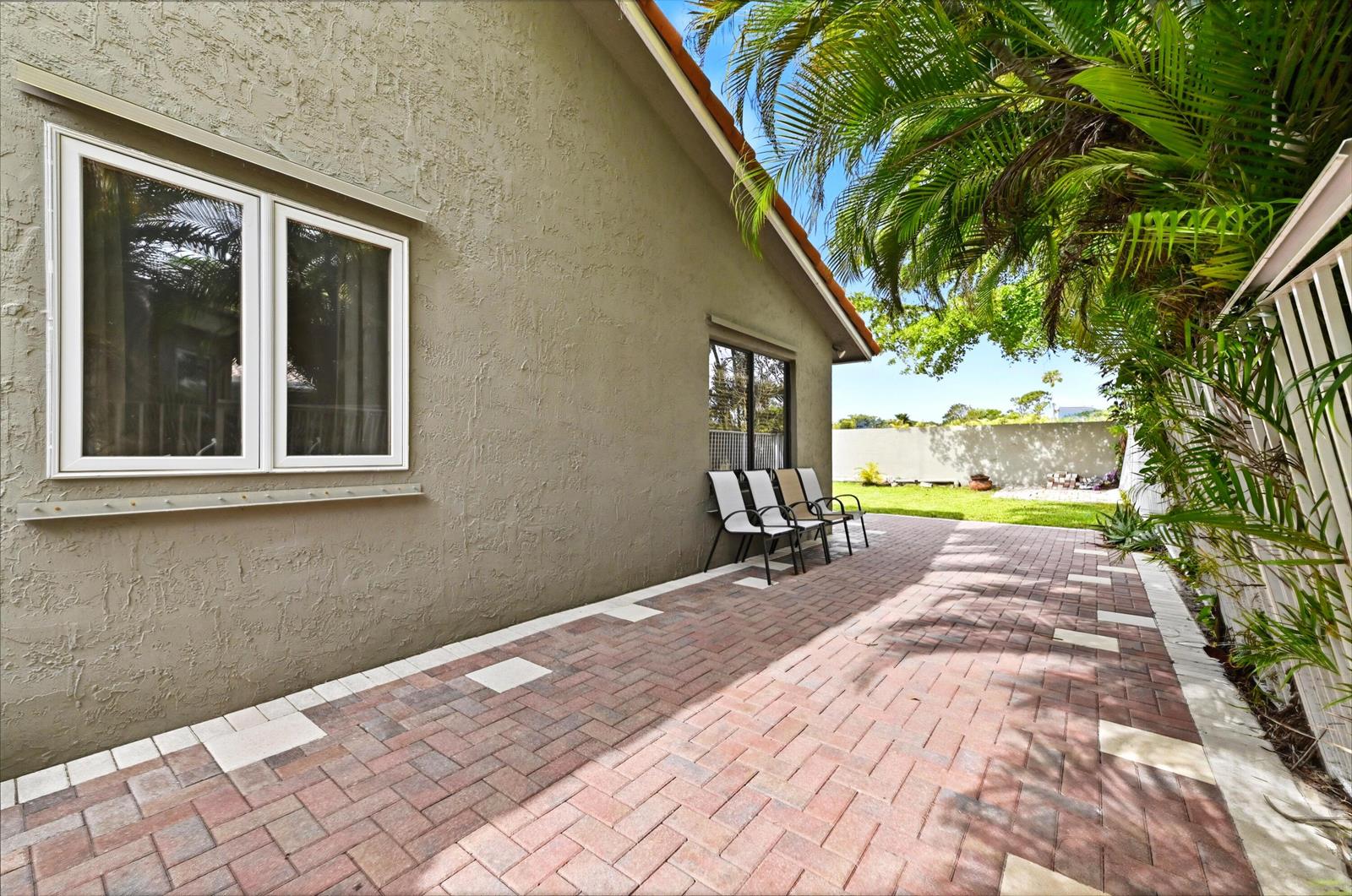 A paved patio sits beside a tan stucco house wall with two windows and chairs — 263 NW 48th Avenue, Deerfield Beach FL 33442, DEERFIELD BEACH, FL