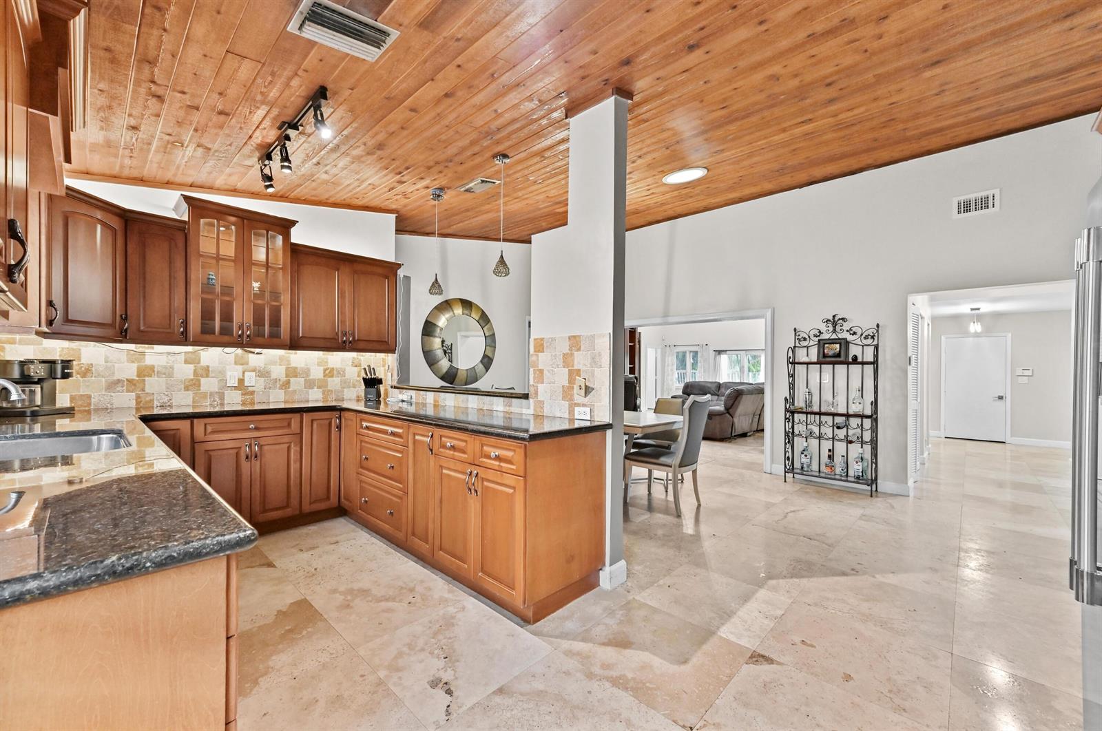 A kitchen with wood cabinets, granite countertops, and a wood-paneled ceiling opens to a dining area — 263 NW 48th Avenue, Deerfield Beach FL 33442, DEERFIELD BEACH, FL