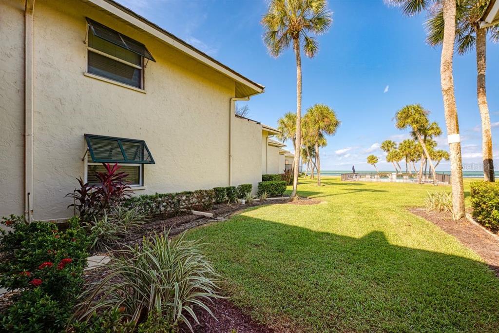 A side view of a beige building exterior with green awnings overlooking a grassy lawn — 4660 OCEAN BOULEVARD UNIT G1, SARASOTA, FL