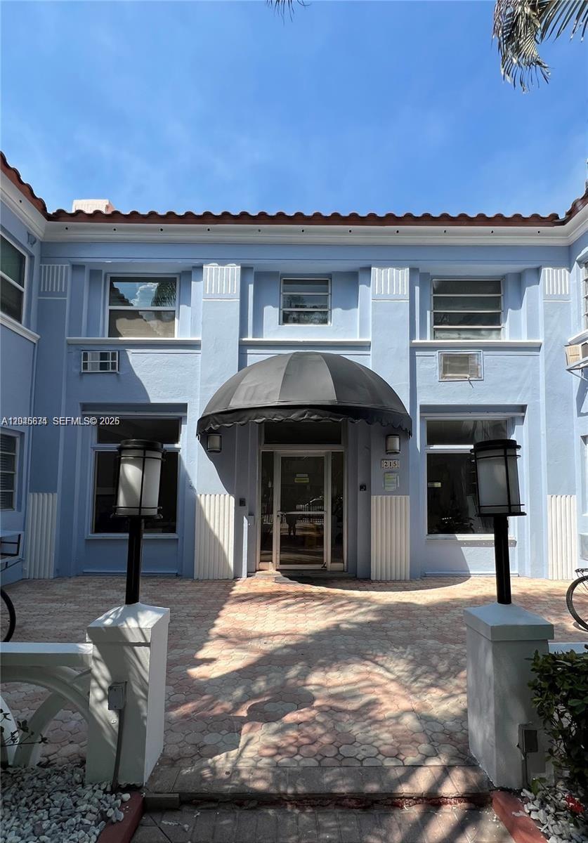 The exterior of a light blue building features a central arched entrance with a canopy — 215 30th St # 22, Miami Beach FL 33140, MIAMI BEACH, FL