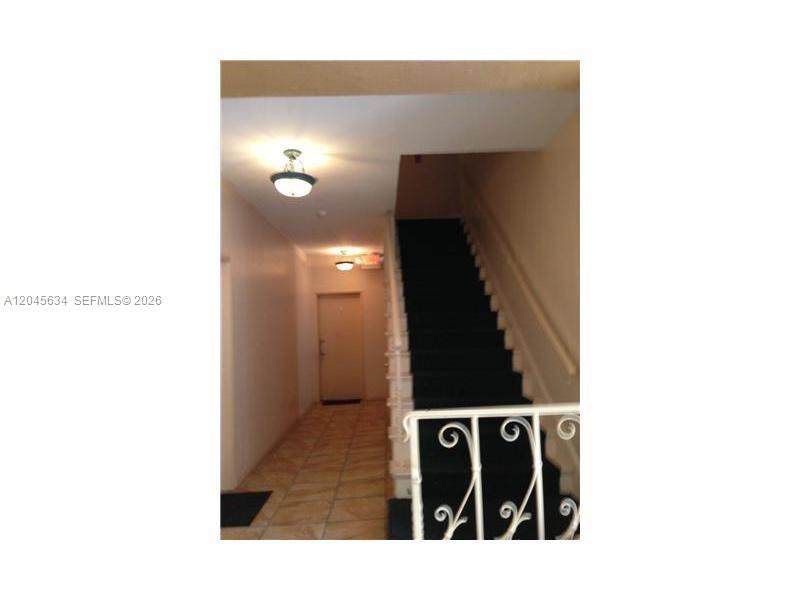 A hallway features tiled flooring, two ceiling lights, and a staircase with a decorative railing — 215 30th St # 22, Miami Beach FL 33140, MIAMI BEACH, FL