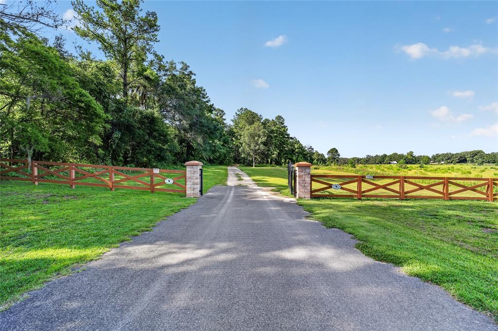 A paved driveway leads through a gated entrance with wooden fencing and brick pillars — 15020 W HIGHWAY 328, OCALA, FL