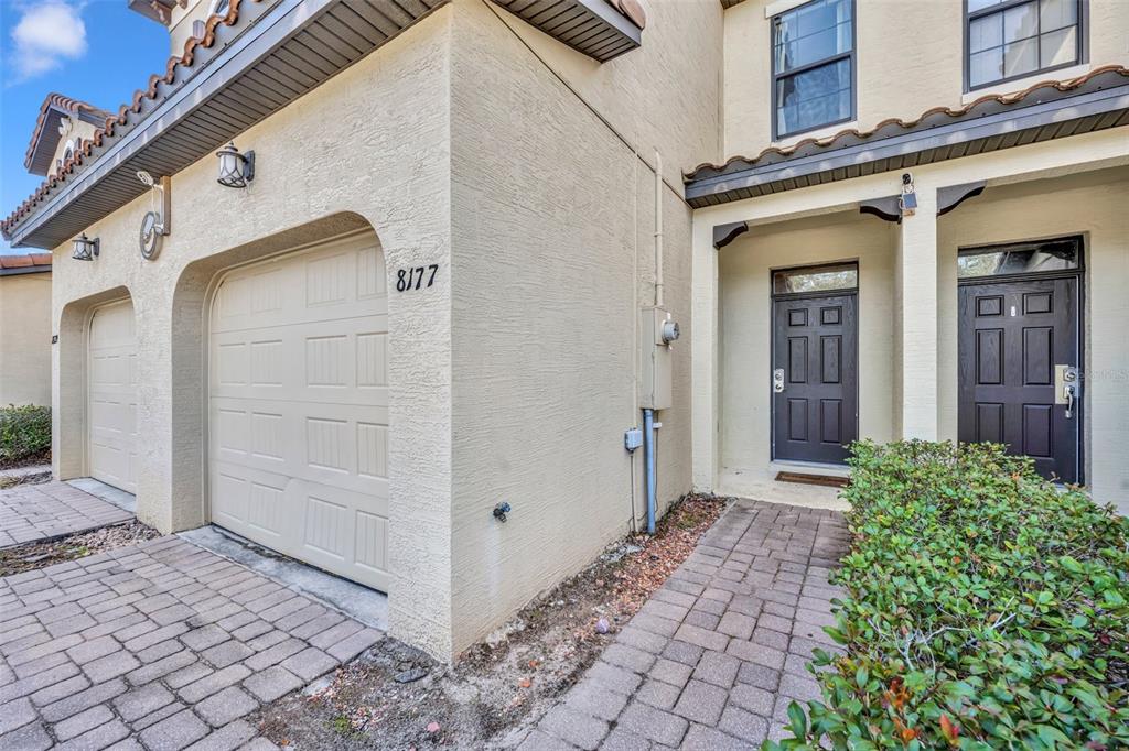 A beige townhouse exterior features a garage, two dark front doors, and a brick walkway — 8177 ROSEVILLE BOULEVARD, DAVENPORT, FL
