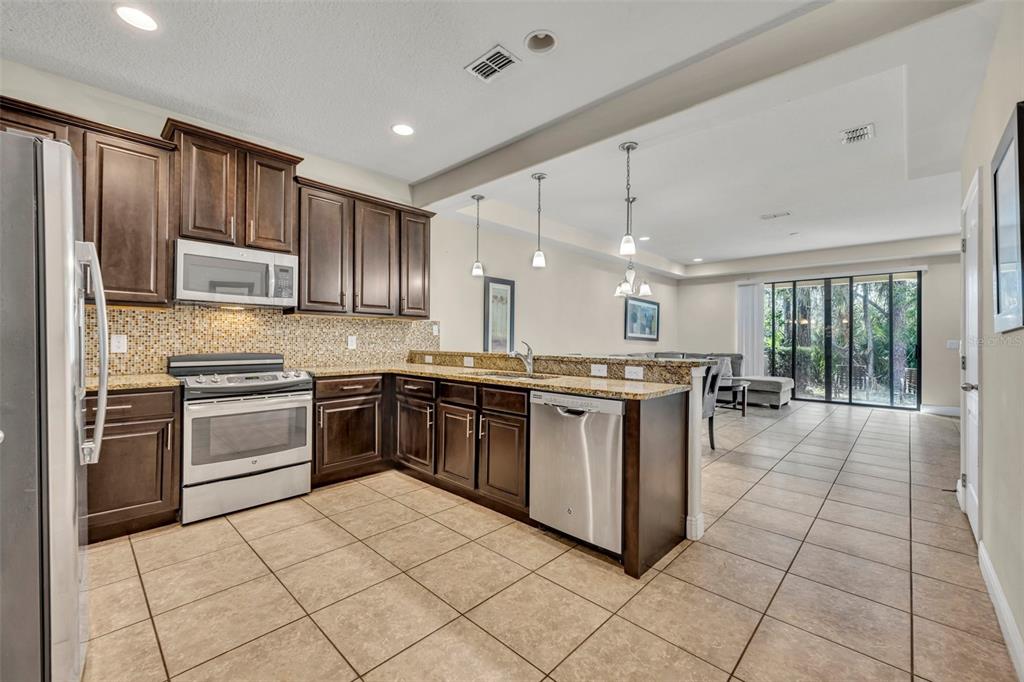 A kitchen with dark wood cabinets, granite countertops, stainless steel appliances, and tile flooring — 8177 ROSEVILLE BOULEVARD, DAVENPORT, FL