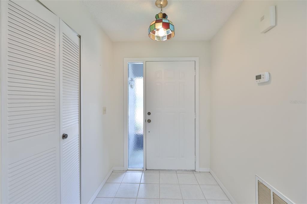 An entryway features white walls, tiled flooring, a louvered closet door, and a stained-glass pendant light — 1616 LAYTON COURT, SUN CITY CENTER, FL
