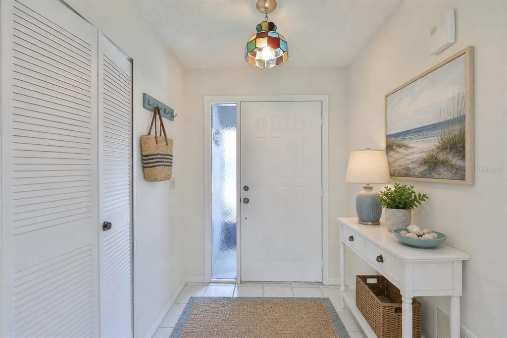 A bright entryway features a white door, a console table, a stained-glass light, and tile flooring — 1616 LAYTON COURT, SUN CITY CENTER, FL