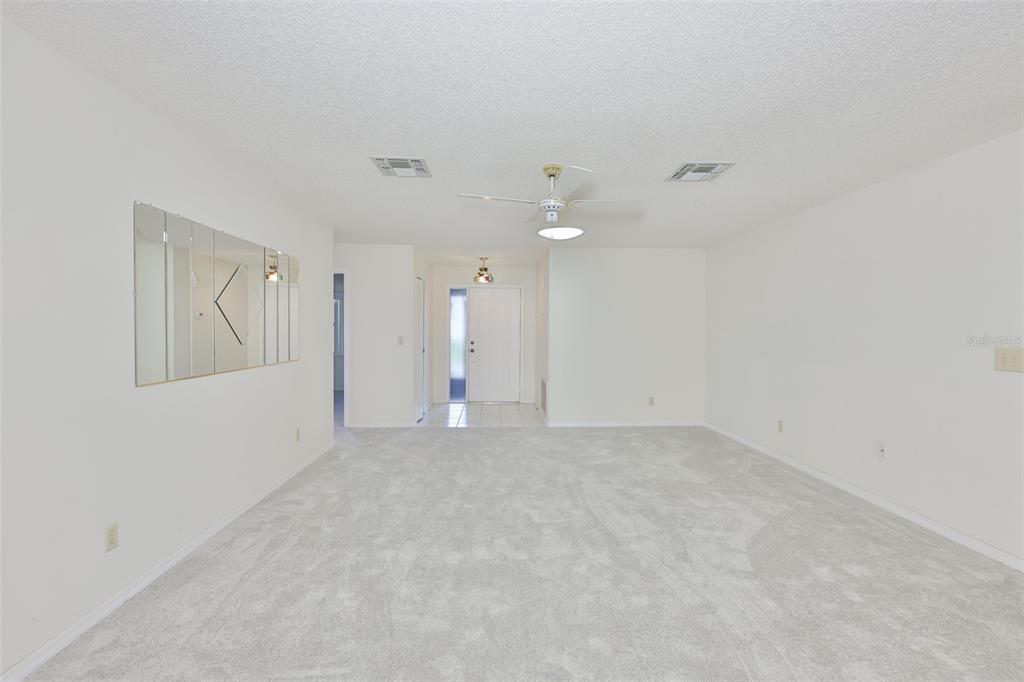 A spacious, carpeted living room features white walls, a ceiling fan, and a mirrored wall — 1616 LAYTON COURT, SUN CITY CENTER, FL