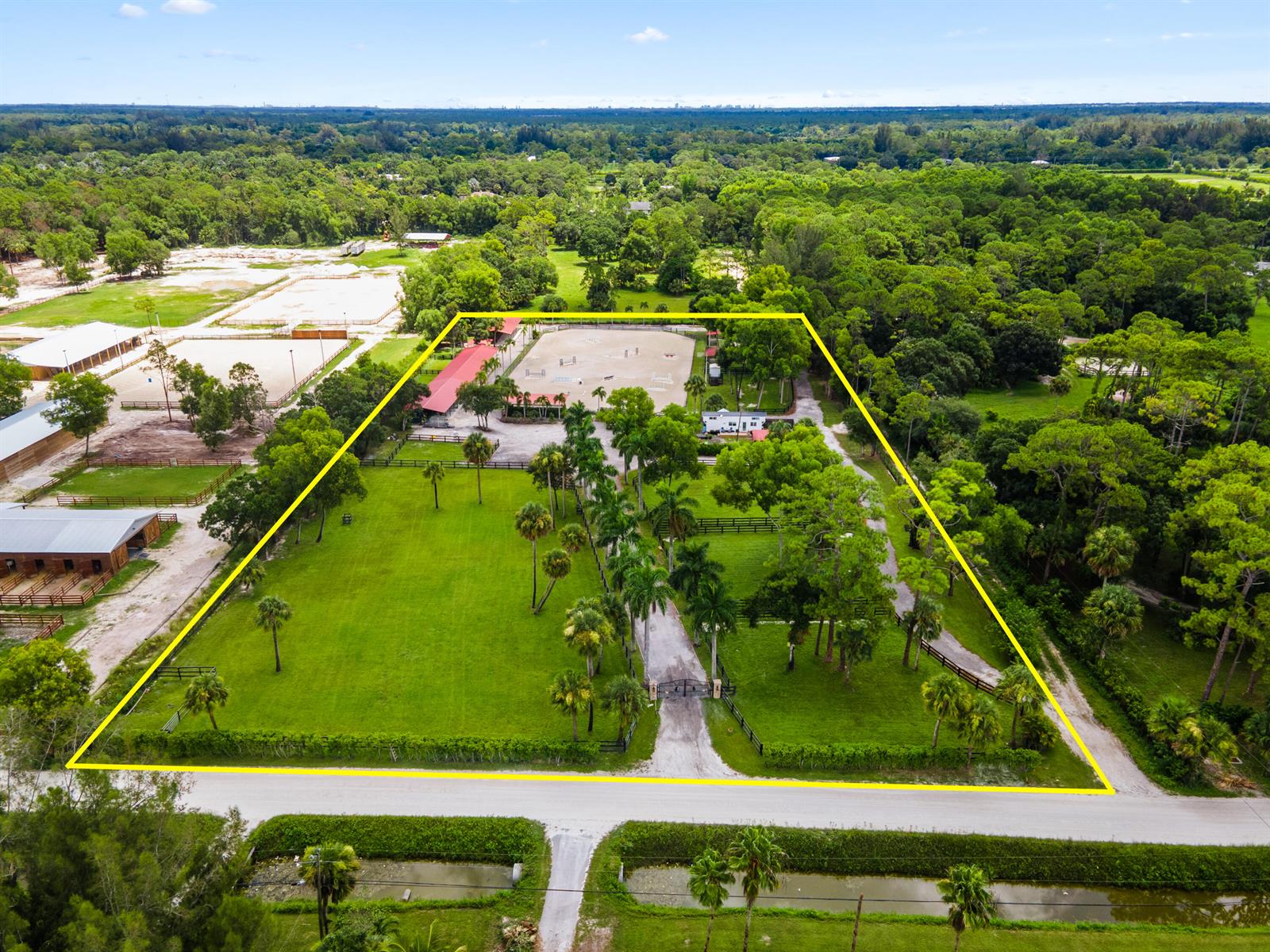 An aerial view shows a fenced equestrian property with a riding arena, stables, and palm trees — 3570 B Road, FL 33470, FL