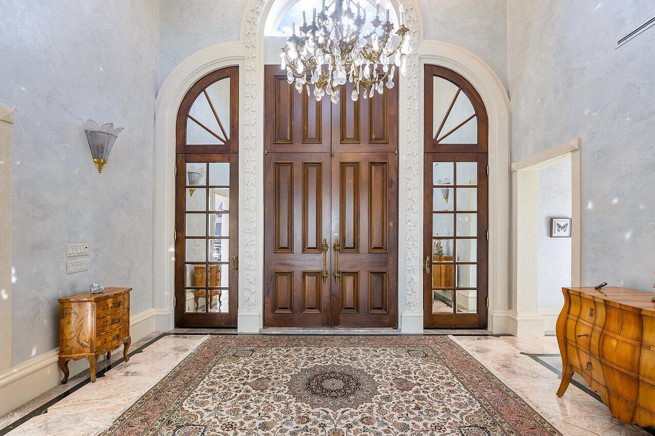 A grand foyer features a large chandelier, double wooden doors, side windows, and marble flooring — 1880 S Ocean Boulevard, Manalapan FL 33462, MANALAPAN, FL