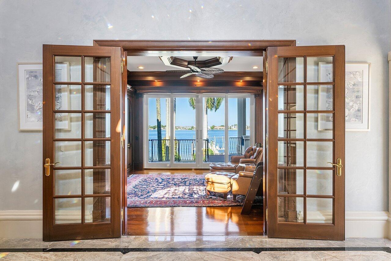 French doors open into a wood-paneled room with a view of a waterfront balcony — 1880 S Ocean Boulevard, Manalapan FL 33462, MANALAPAN, FL