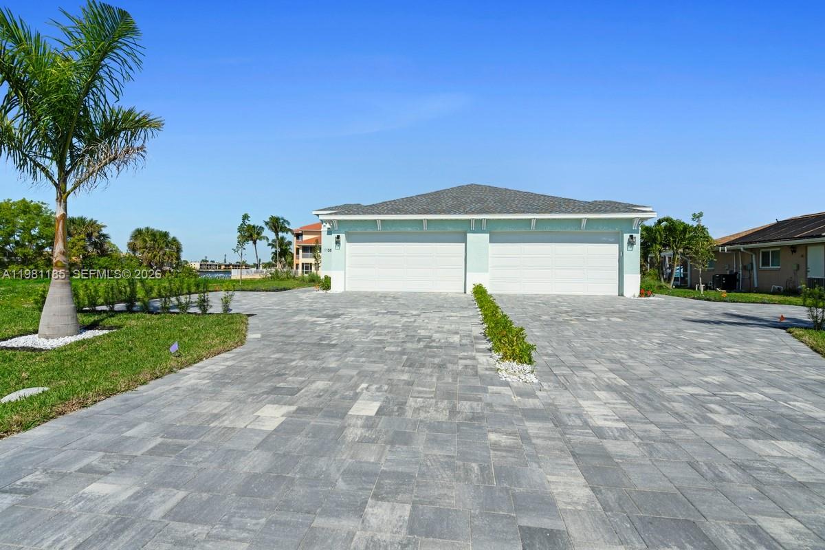 A wide paved driveway leads to a two-car garage of a light-colored house — 1107 SE 38 ST, Cape Coral FL 33904, CAPE CORAL, FL