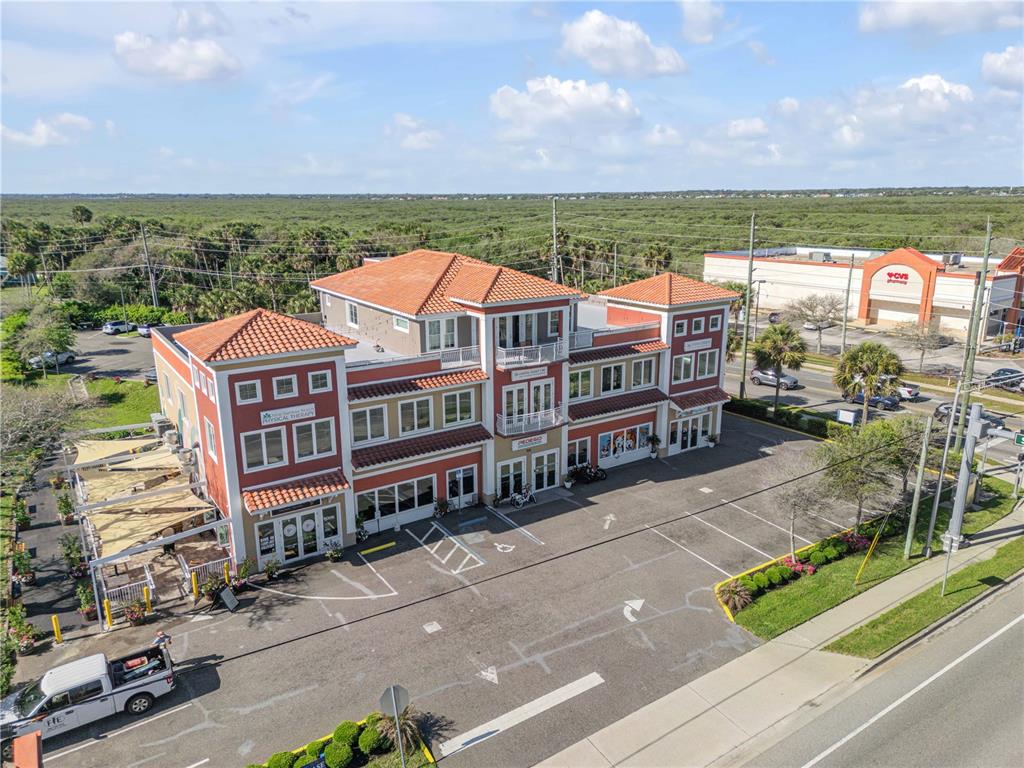An aerial view of a three-story commercial building with a tiled roof and parking lot — 701 E 3RD AVENUE UNIT 4, NEW SMYRNA BEACH, FL