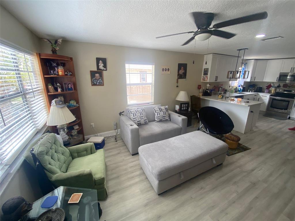 A living room with light wood-look flooring, a gray loveseat, and an open-concept kitchen — 8503 N 11TH STREET, TAMPA, FL