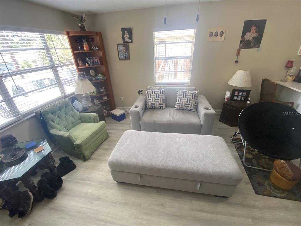 A living room features light wood-look flooring, a gray loveseat, a green armchair, and an ottoman — 8503 N 11TH STREET, TAMPA, FL