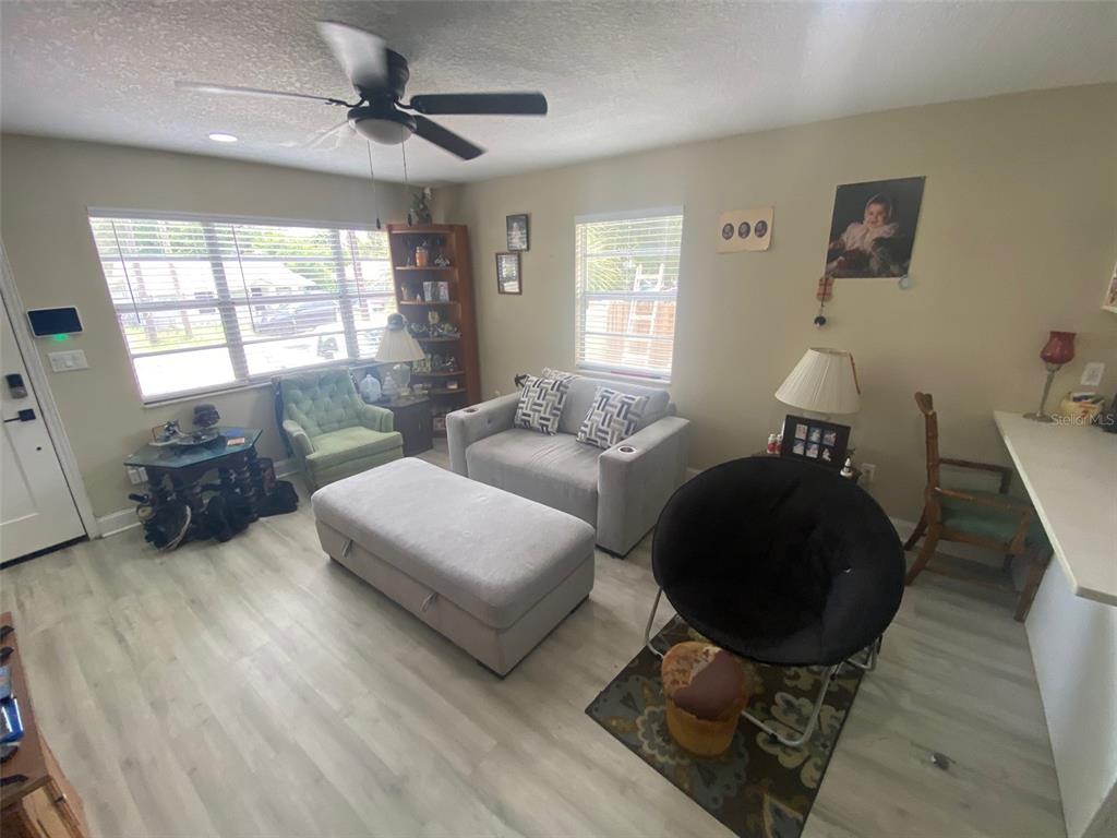 A living room features light wood-look flooring, a gray sofa, an ottoman, and a ceiling fan — 8503 N 11TH STREET, TAMPA, FL