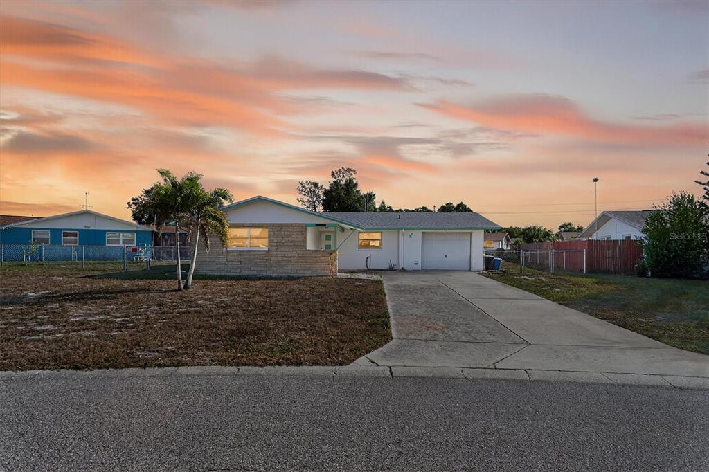 A single-story house with a stone facade, attached garage, and driveway under a sunset sky — 7608 REDCOAT AVENUE, PORT RICHEY, FL