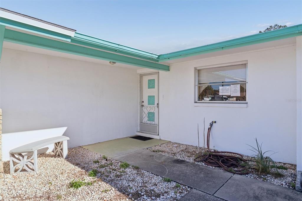 The exterior of a house features a white wall, a turquoise roof trim, and a bench — 7608 REDCOAT AVENUE, PORT RICHEY, FL