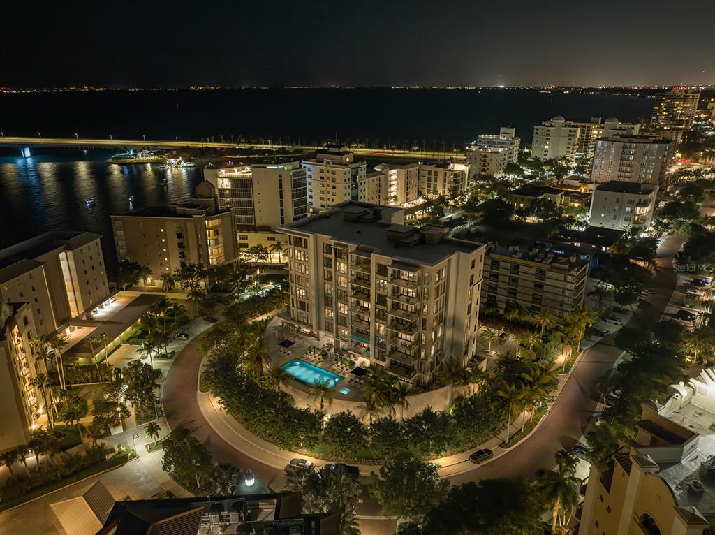 An aerial night view of a multi-story apartment building with a pool and circular driveway — 325 GOLDEN GATE POINT UNIT 401, SARASOTA, FL