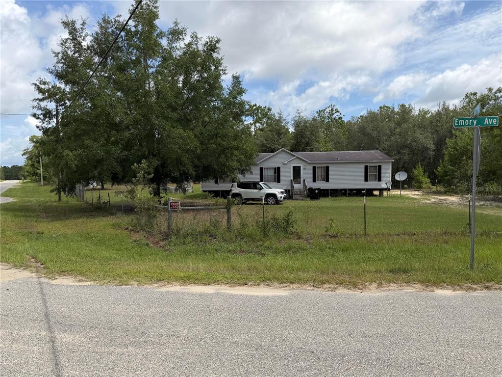 A single-story manufactured home sits on a grassy lot behind a wire fence — 6274 EMORY AVENUE, KEYSTONE HEIGHTS, FL