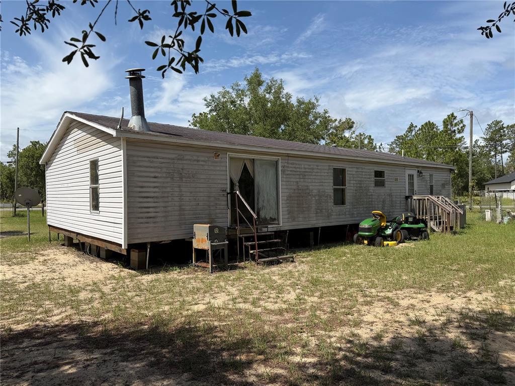 A single-story manufactured home with vinyl siding sits on a sandy lot with lawnmowers — 6274 EMORY AVENUE, KEYSTONE HEIGHTS, FL