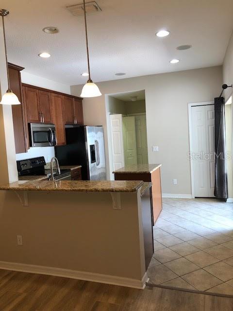 A kitchen features wooden cabinets, a granite breakfast bar, and stainless steel appliances — 6344 LAKE SMITH CIRCLE, WINDERMERE, FL