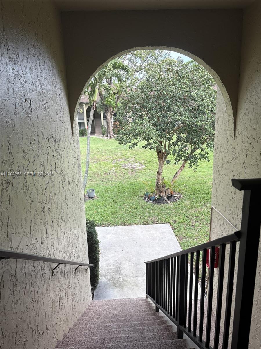 An outdoor staircase leads down from a covered archway to a grassy courtyard with trees — 721 Sunny Pine Way # C2, Green Acres FL 33415, GREEN ACRES, FL