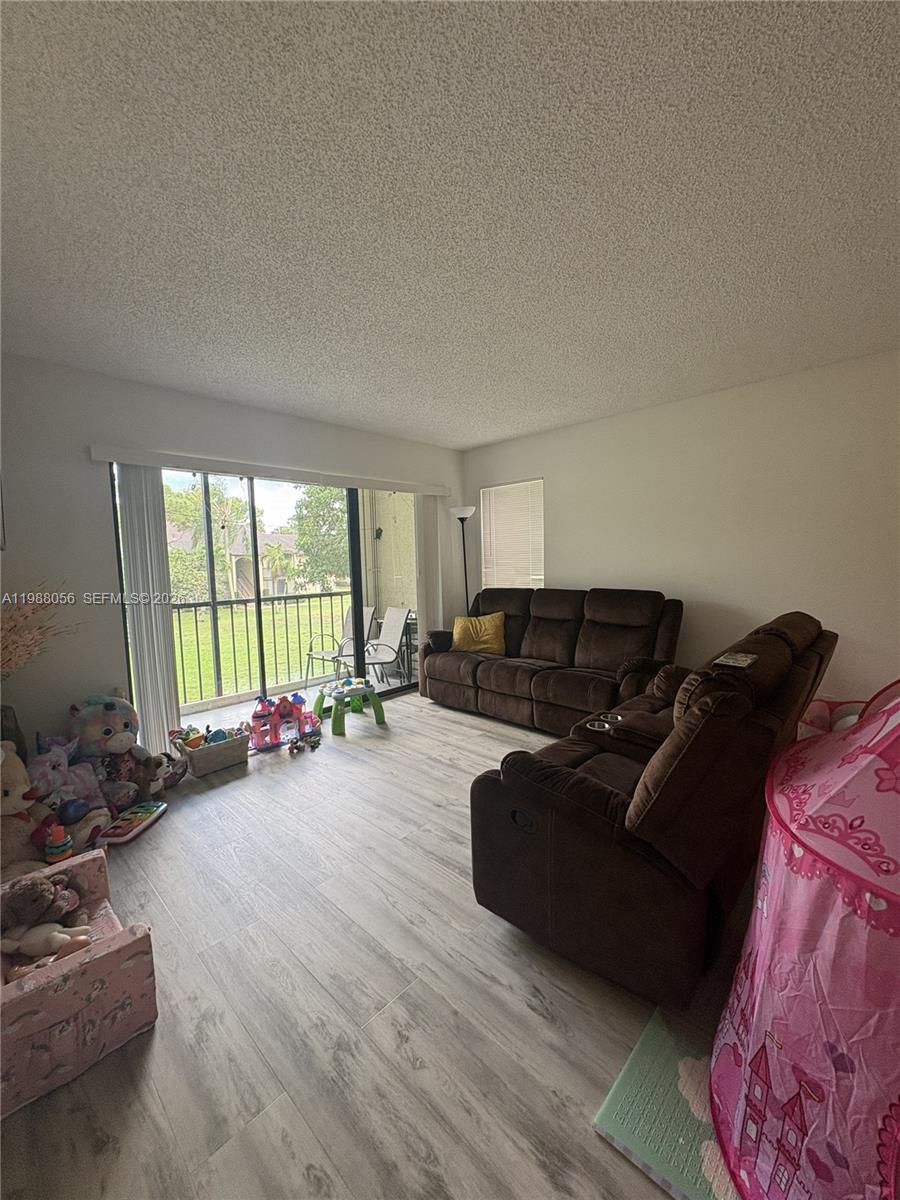 A living room features wood-look flooring, brown sofas, a balcony, and children's toys — 721 Sunny Pine Way # C2, Green Acres FL 33415, GREEN ACRES, FL
