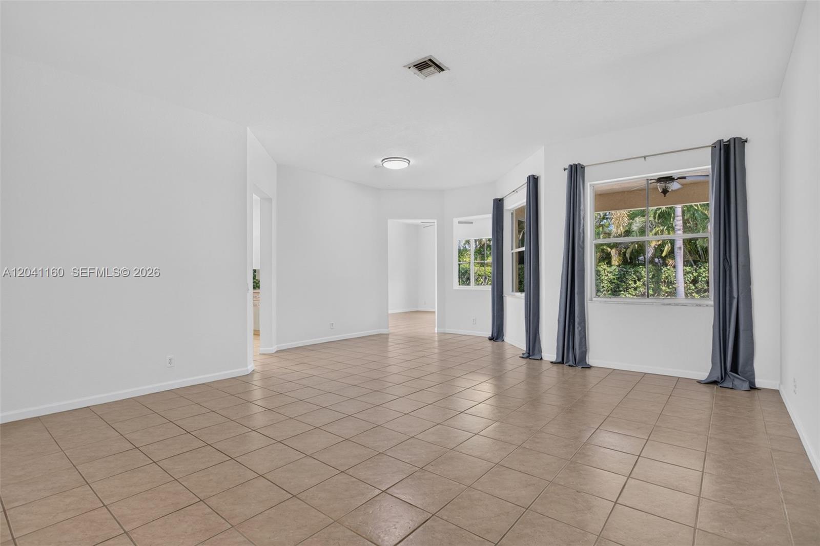 An empty room features beige tile flooring, white walls, and windows with gray curtains — 786 Nandina Dr, Weston FL 33327, WESTON, FL