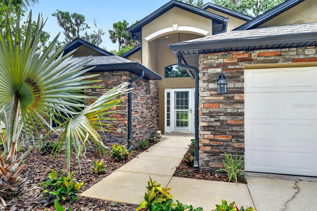 A stone-veneer house exterior features a concrete walkway leading to a white front door — 31 WILD CAT LANE, ORMOND BEACH, FL