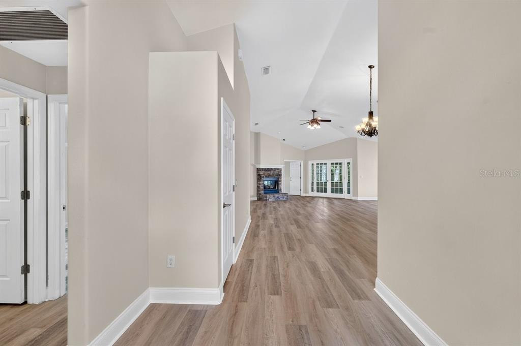 A hallway with light wood-look flooring leads into a living area with a vaulted ceiling — 31 WILD CAT LANE, ORMOND BEACH, FL