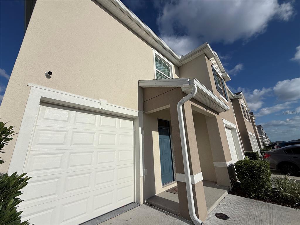 A two-story townhouse exterior features a white garage door, a blue front door, and beige stucco — 2354 TAY WES DRIVE, ST CLOUD, FL