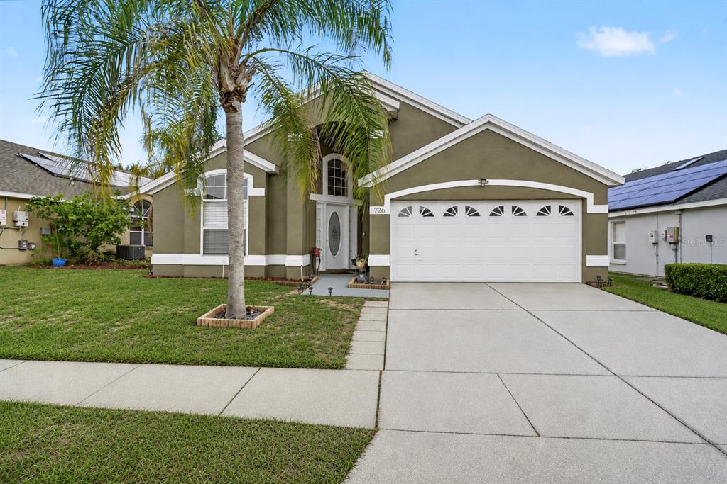 A single-story house with a green stucco exterior, a two-car garage, and a palm tree — 726 ROCHESTER LOOP, DAVENPORT, FL