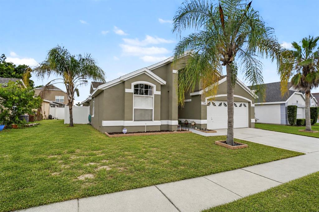 A single-story house with olive-green stucco siding, a two-car garage, and two palm trees — 726 ROCHESTER LOOP, DAVENPORT, FL