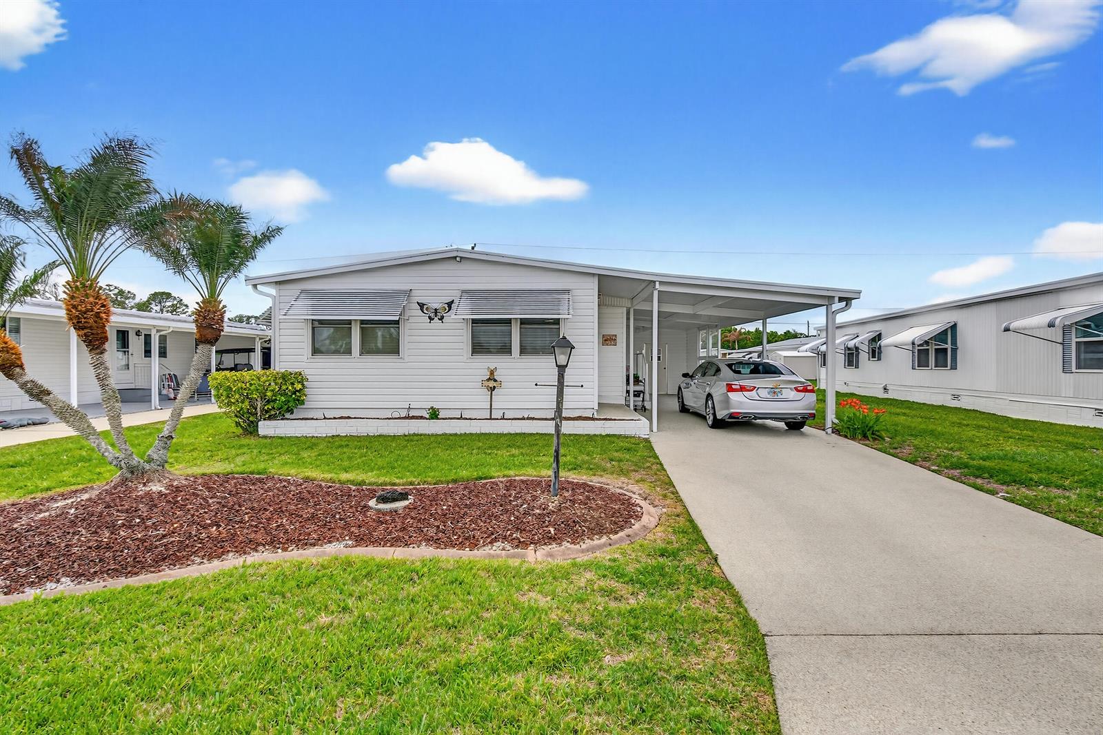 A single-story white mobile home features a concrete driveway, carport, and a palm tree — 1520 St Thomas Avenue, Sebring FL 33870, SEBRING, FL