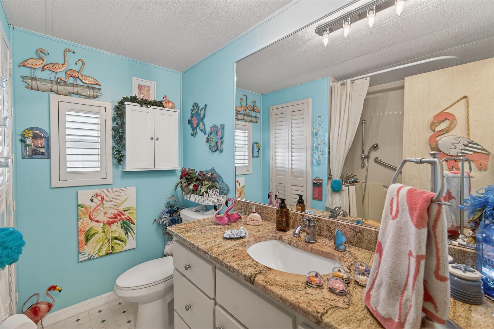 A bathroom features light blue walls, a granite vanity, and flamingo-themed decor — 1520 St Thomas Avenue, Sebring FL 33870, SEBRING, FL