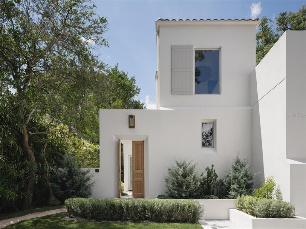 A modern white stucco house features a wooden front door, tall windows, and landscaped gardens — 1150 VIA SALERNO, WINTER PARK, FL