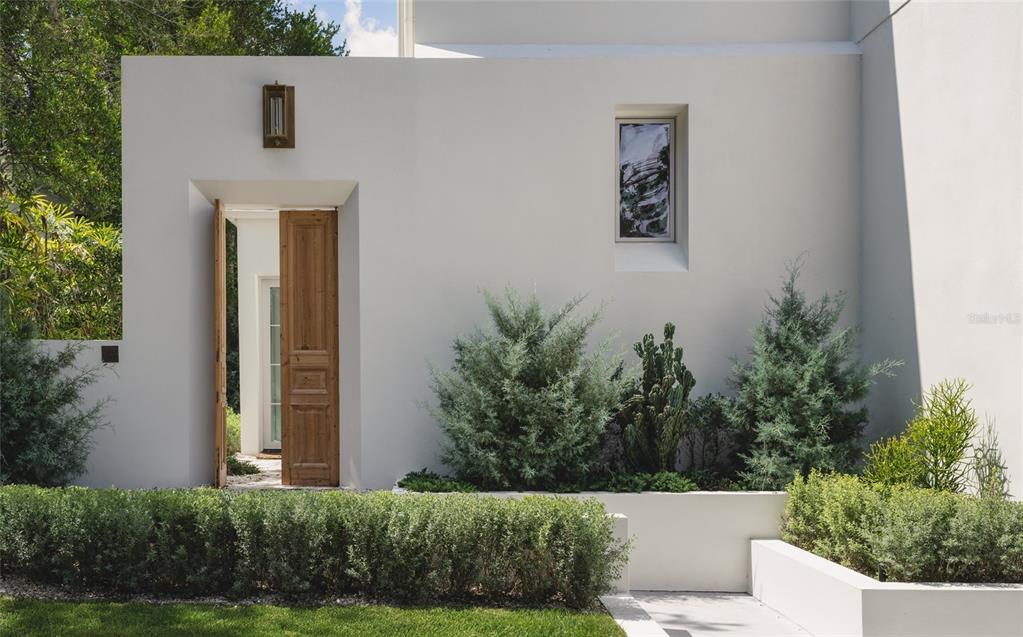 A stone path leads through open wooden doors to a white building with glass doors — 1150 VIA SALERNO, WINTER PARK, FL