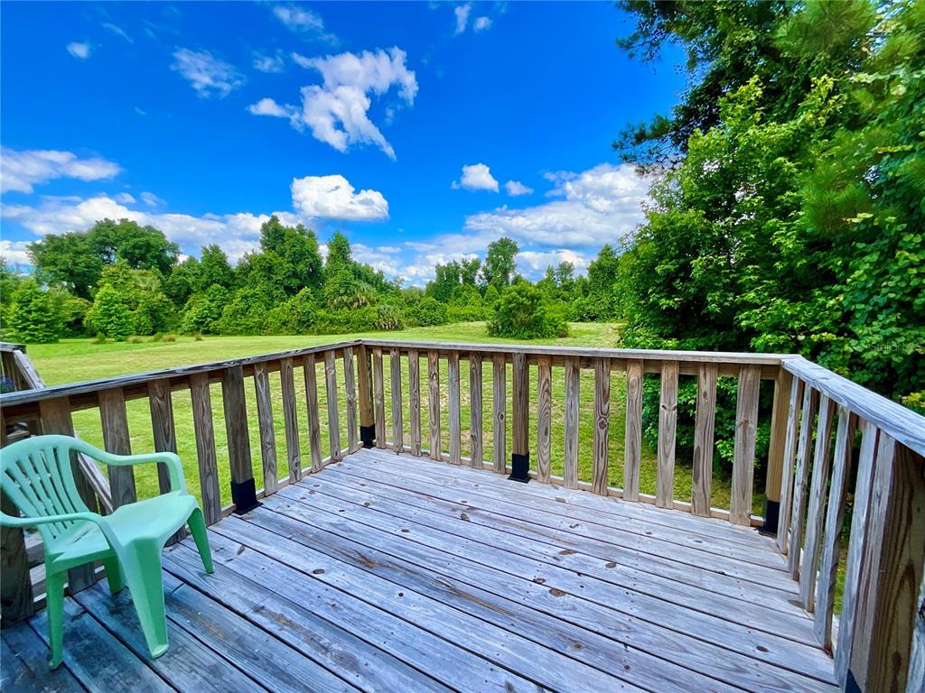 A wooden deck with a green plastic chair overlooks a grassy field and trees — 122 TANNER ROAD, FLORAHOME, FL