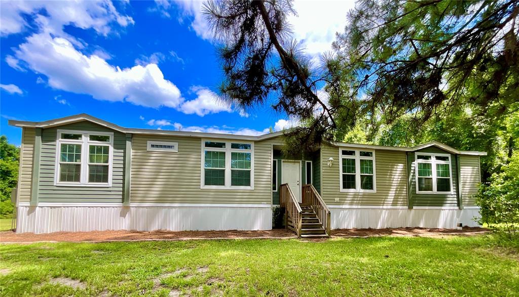 A light green manufactured home with white skirting and a wooden front porch entrance — 122 TANNER ROAD, FLORAHOME, FL