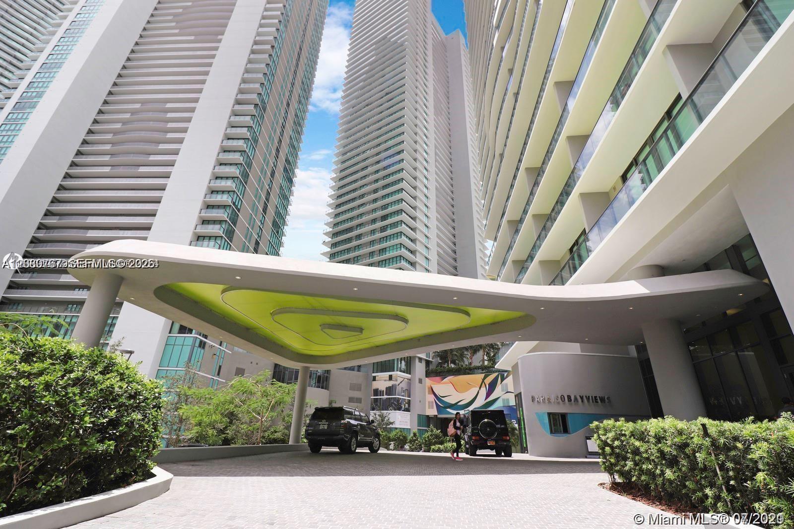 The exterior of a modern high-rise building features a large, lime-green geometric porte-cochère — MIAMI, FL