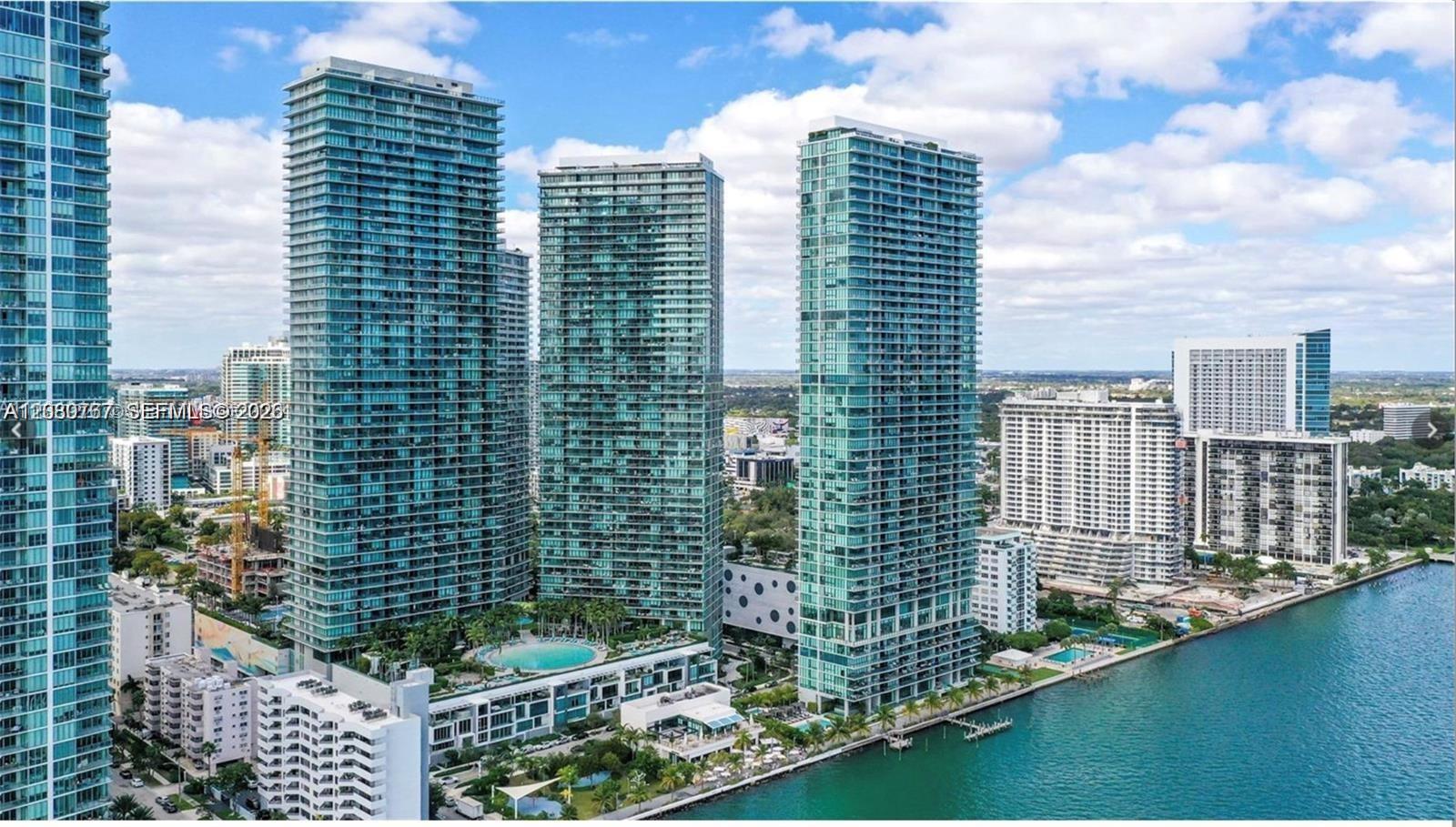 An aerial view of several tall glass residential towers situated along a waterfront — MIAMI, FL